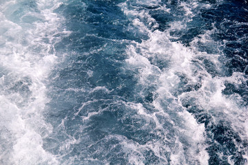 Turbulence made by foam of sea water from a high-speed yacht on surface of sea. Blue sea waves with lot of sea foam. Surface of sea with waves, splash, foam and bubbles, blue background and wallpaper.