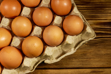 Raw chicken eggs in cardboard pack on wooden table