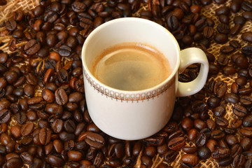 White cup of coffee on coffee beans in background.