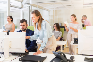 Business woman explaining something to male coworker, pointing at computer