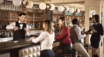 Barman is servicing young people who are relaxing in bar indoor.