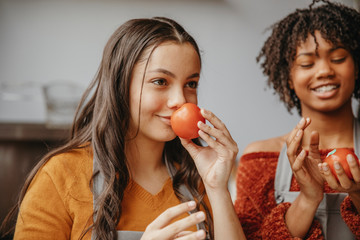 Smiling teenage girls smelling tomatoes in cooking class