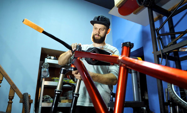 A young male mechanic in his workshop assembles a bicycle