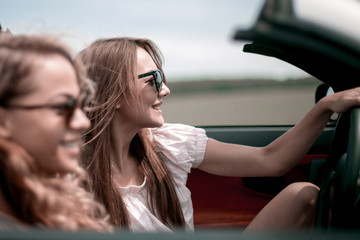 two fashionable girls travel in a convertible car.