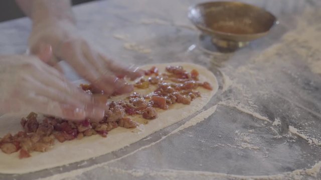 Chef hands making turkish arab food fatayer in modern restaurant kitchen close up. Man puts roasted meat with vegetables on the dough preparing it for baking. Turkish food preparation