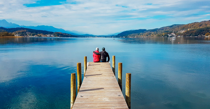 Couple sitting and hugging at the pier by W&ouml;rtersee, P&ouml;rtschach, Austria. Beautiful lake landscape, surrounded by Alps. This lake is natural drinking water tank. Love is in the air. Romantic moments.