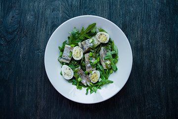 Marinated herring with arugula, onions, boiled quail eggs and lemon juice and olive oil. Delicious salad. Proper nutrition. Dark wooden background.