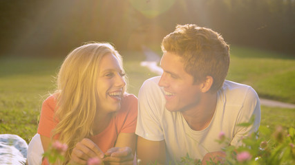 LENS FLARE: Couple lying in the grassfield laughs while filming a video blog.