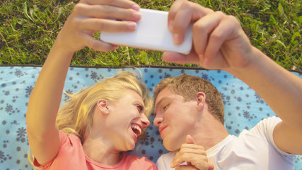 CLOSE UP: Happy girl laughs as man is about to kiss her while lying on blanket.