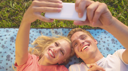 CLOSE UP: Playful young couple lying on a comfy blanket and taking selfies.
