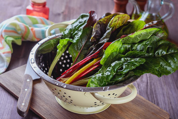 A lot of colorful eaves of chard are drained in a colander after has been rinsed in cold water to prepare salad with others ingridients