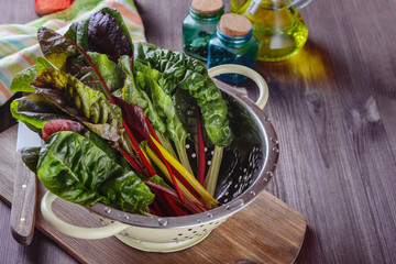 A lot of colorful eaves of chard are drained in a colander after has been rinsed in cold water to prepare salad with others ingridients