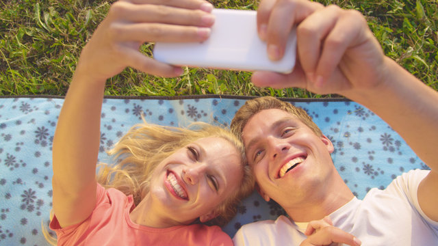 CLOSE UP: Playful young couple lying on a comfy blanket and taking selfies.