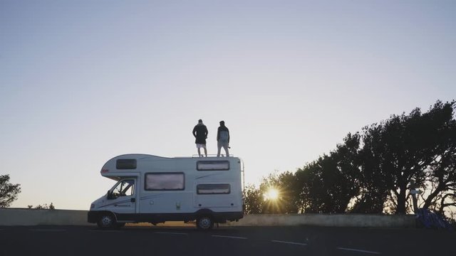 Men on camper van on road and blue sky at sunset 