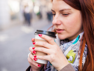 Woman holding coffee cupon the blurred street. Sunny spring afternoon. Red manicure