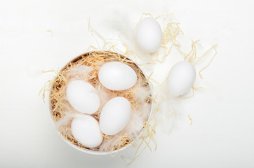 Eggs in a round box with hay on a white background. Concept easter composition, spring holiday, healthy food. Top view, flat lay.