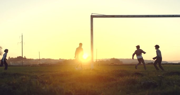 Football playing of the rural children on the field near the village on the beautiful sunset. Outdoor.