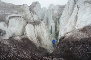 A free climber with an ice ax stands at the foot of the Great Glacier next to epic crack in fog in...