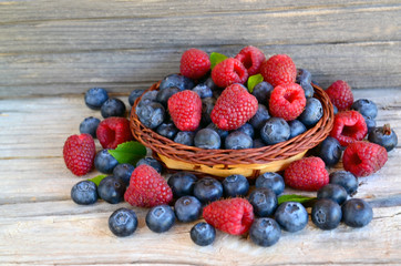Freshly picked organic raspberries and blueberries in a basket on old wooden background.Blueberry and raspberry. Healthy eating,summer fruits or diet concept.Selective focus.