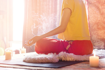 A girl surrounded by candles at home at the window meditates in the lotus position making fingers...