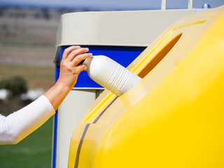 A mature woman pulling a plastic bottle in a yellow bin for recycling plastic