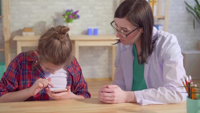 doctor psychologist teaches an autistic child to use a smartphone