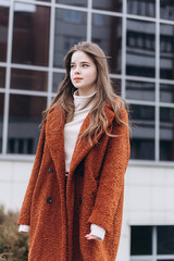 Outdoor urban portrait of cheerful beautiful caucasin young girl in coat. Casual style concept