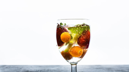 glass with transparent liquid and fresh fruits floating on a white background