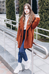 Outdoor urban portrait of cheerful beautiful caucasin young girl in coat. Casual style concept