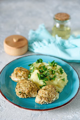 Mashed potatoes with meatballs in a creamy sauce with greens on a gray background