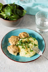 Mashed potatoes with meatballs in a creamy sauce with greens and a fork on the background of a dish with spinach and a glass of water