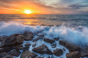 Stunning seascape with the colorful sunrise sky and beauty waves at the rocky coastline of the Black Sea