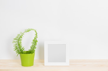 White picture frame and fern in green pot