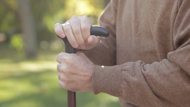 Closeup of shaking man's hands leaning on cane. Alzheimer symptoms, tremor
