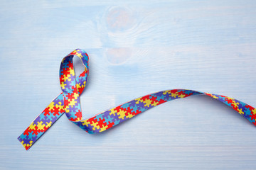 World Autism awareness and pride day with Puzzle pattern ribbon on blue wooden background