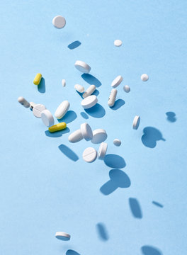 Pills and capsules falling on a blue surface