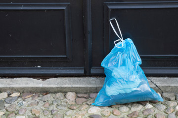 blue plastic garbage bag in the garden, in front of black door