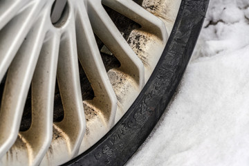 Close up of winter tire, aluminium car rim, dirty from dust and oil, snow next to it