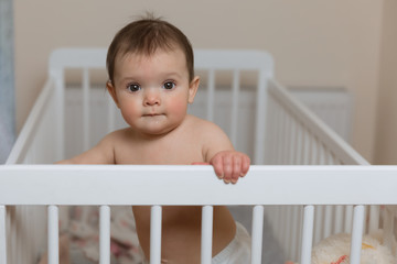 Baby girl in a diaper playing in the crib.