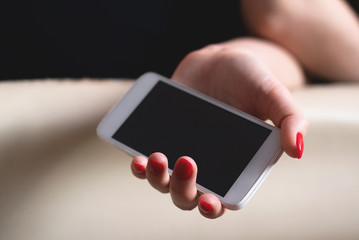 Tired woman is sleeping on a sofa with a blank screen mobile phone in her hand. Close up.