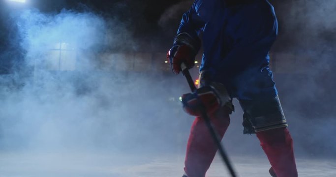Professional hockey player with a stick and a puck moves on Luda in skates and helmet on a dark background and smoke. Dribbling with the puck of a young man on the ice arena