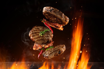 Flying beef hamburgers pieces above burning grill - obrazy, fototapety, plakaty
