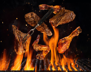 Flying beef steaks and chicken pieces above grill
