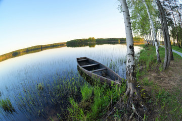 Old wooden boat at the shore of a forest lake. Idialistic landscape with spring nature and clear blue sky