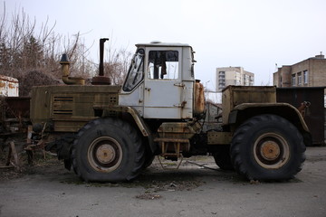 A large, rusty, old tractor on the territory of an abandoned factory.