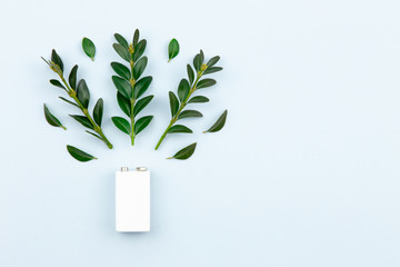 Eco energy or green power illustration with a white battery and sprigs leaves on a light background with copy space for text.