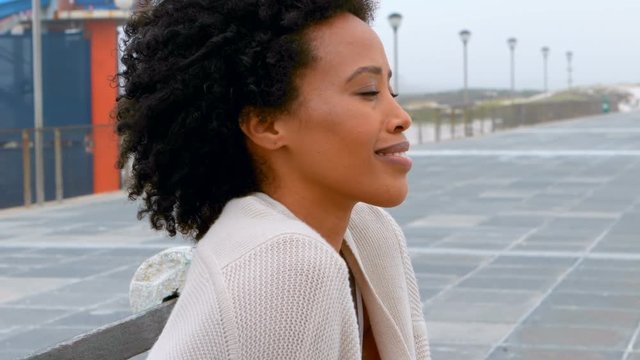 Thoughtful young African american woman sitting on bench at promenade 4k