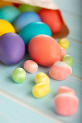 Easter colorful dyed chicken eggs in a paper bag and sweets on a blue wooden table..