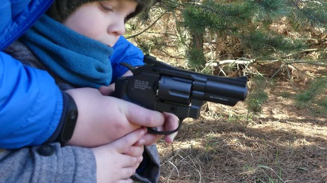 A child with a gun suggests a target. A little boy shoots a pneumatic pistol. Pneumatic revolver in hand. Close-up.