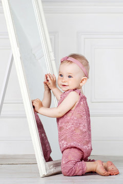 Little pretty girl plays with a big mirror